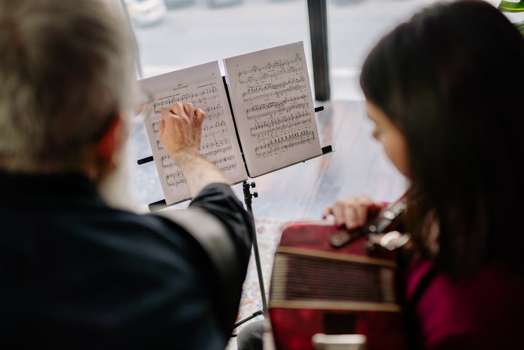 An adult teaching a student music, pointing at sheet music indoors.